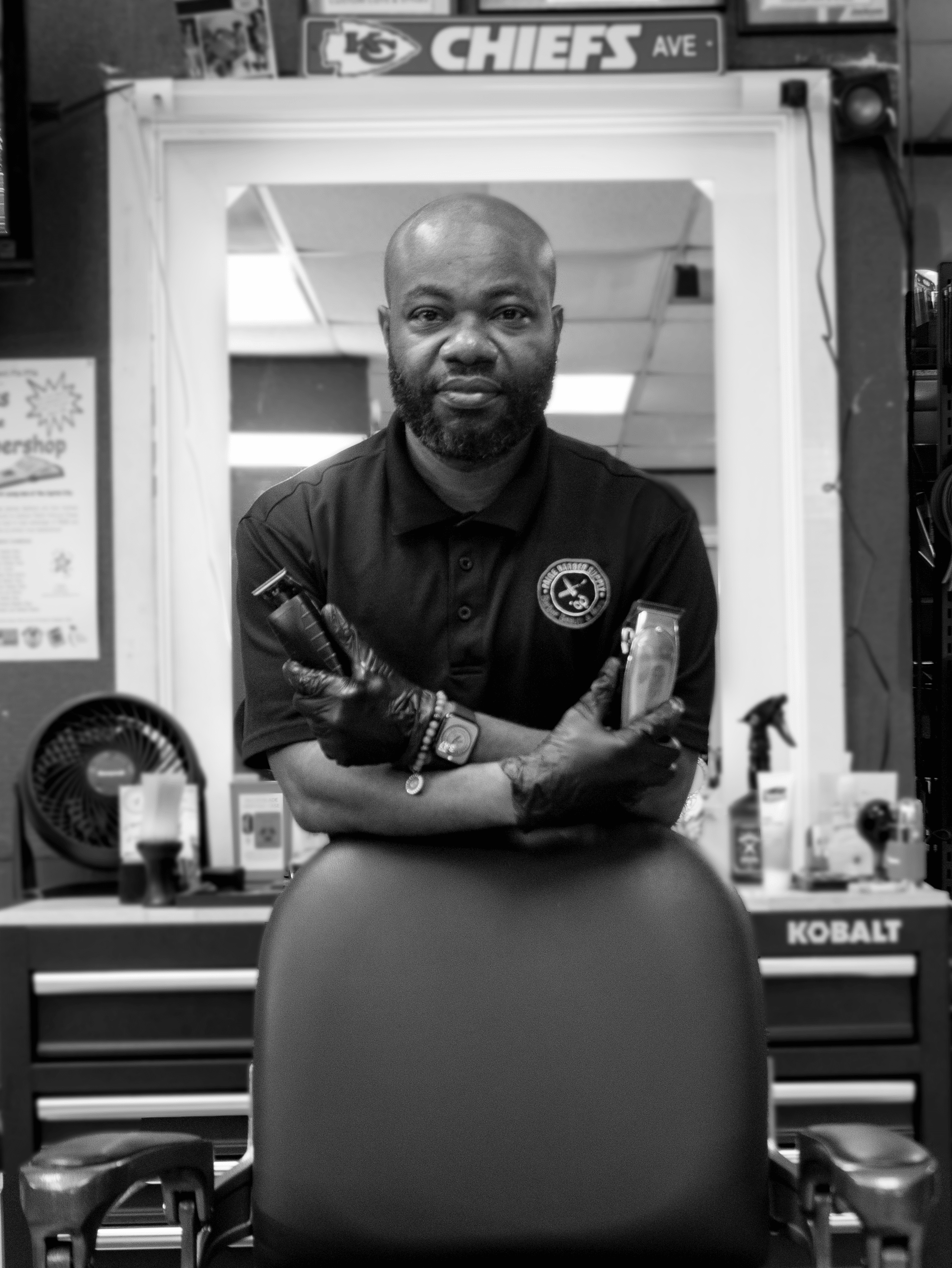 Chris Paige standing behind a barber's chair holding a pair of clippers.